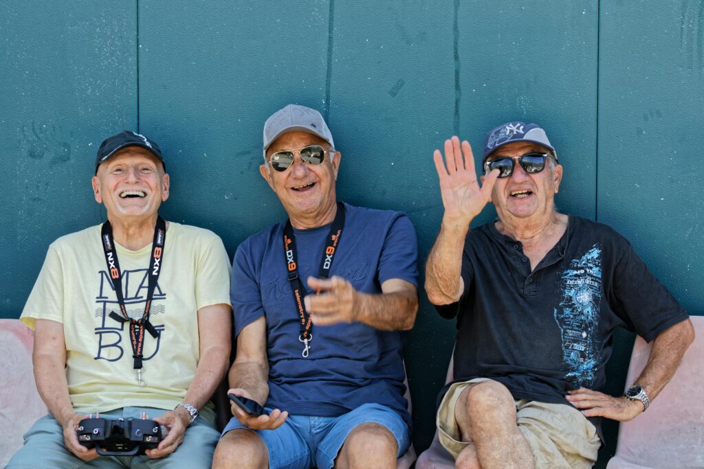 Three senior men smiling, wearing hats and sunglasses, having a good time outdoors.